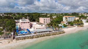 An aerial view of a coastal hotel with a swimming pool, beach, and ocean. - Butterfly Beach Hotel (Oistins)