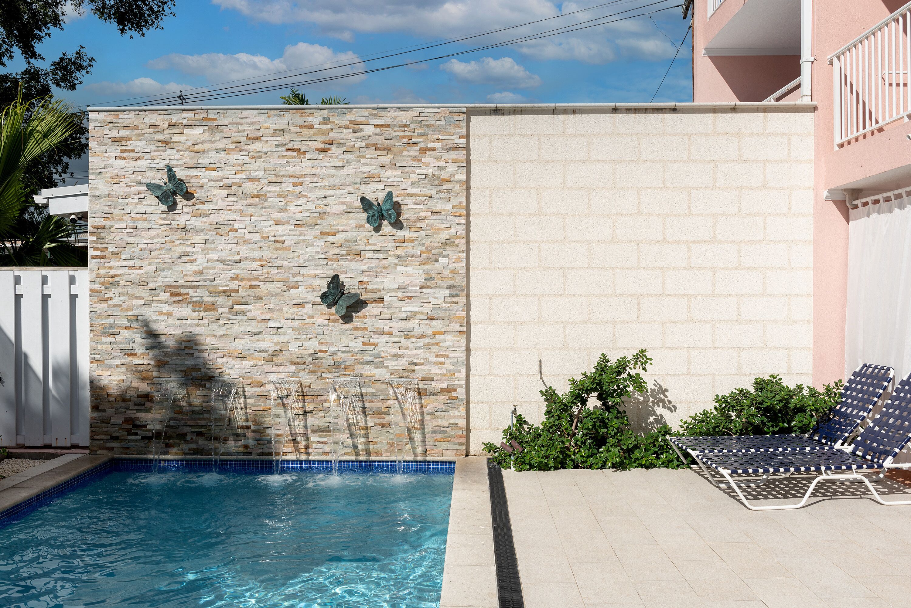Una piscina con un muro de piedra y decoraciones de mariposas, una valla blanca y un balcón con barandilla.