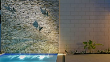 Una piscina con un muro de piedra y esculturas de mariposas, además de un muro de ladrillo blanco y una planta.