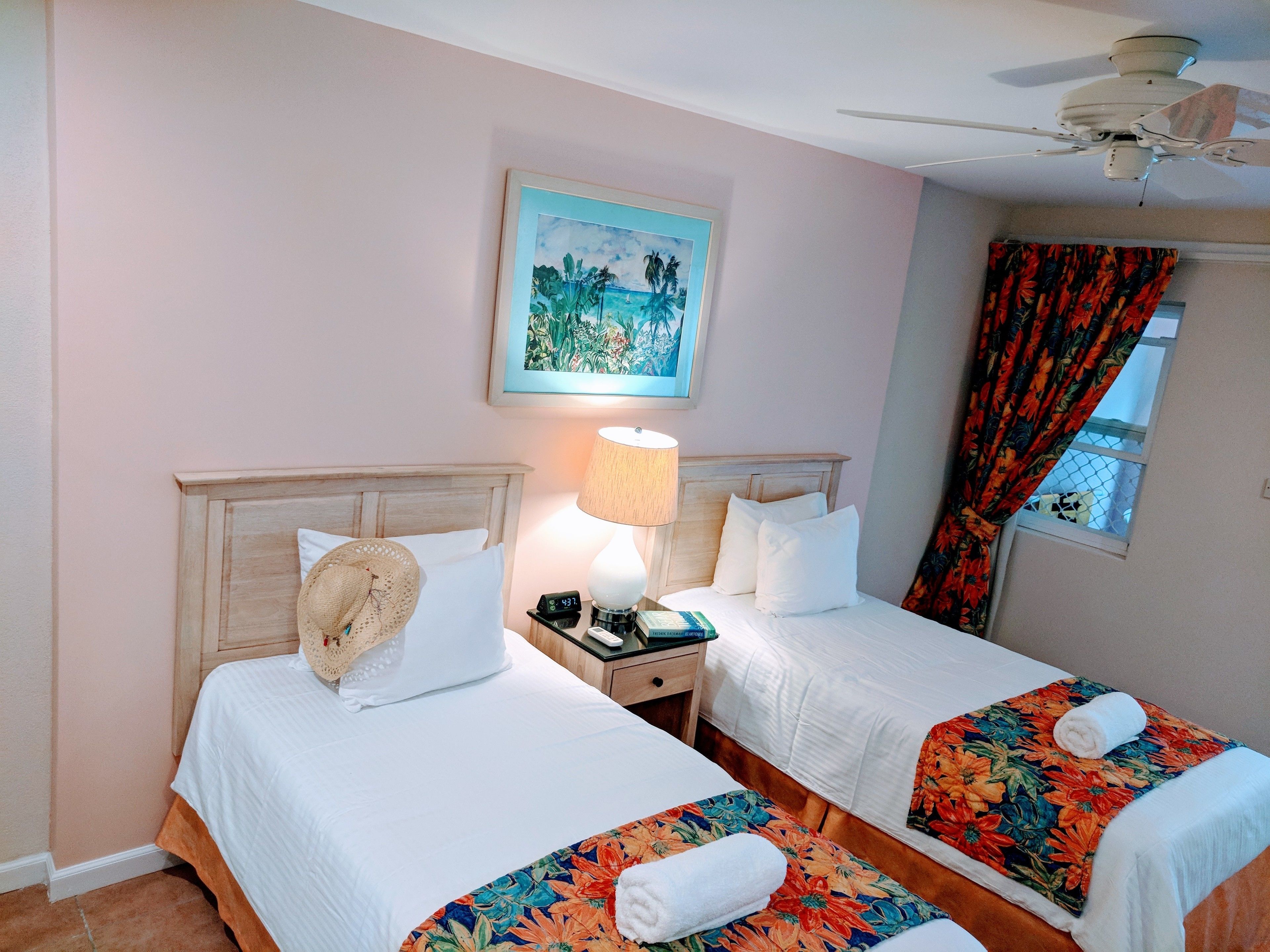 A hotel room with two beds, a nightstand, a lamp, a painting, and a window with curtains.
