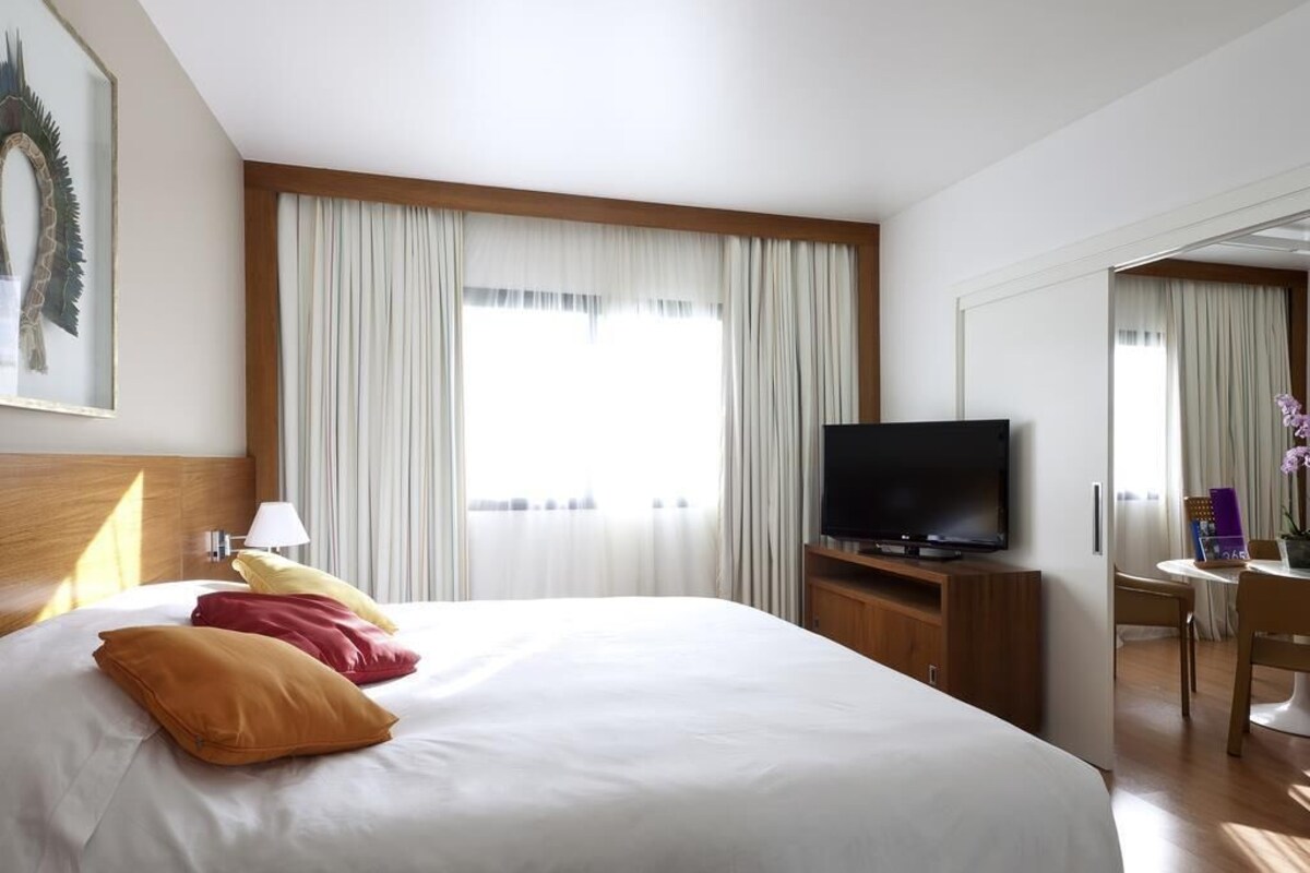 Une chambre d’hôtel comprenant un lit, une télévision, un bureau avec une chaise et une fenêtre avec des rideaux.