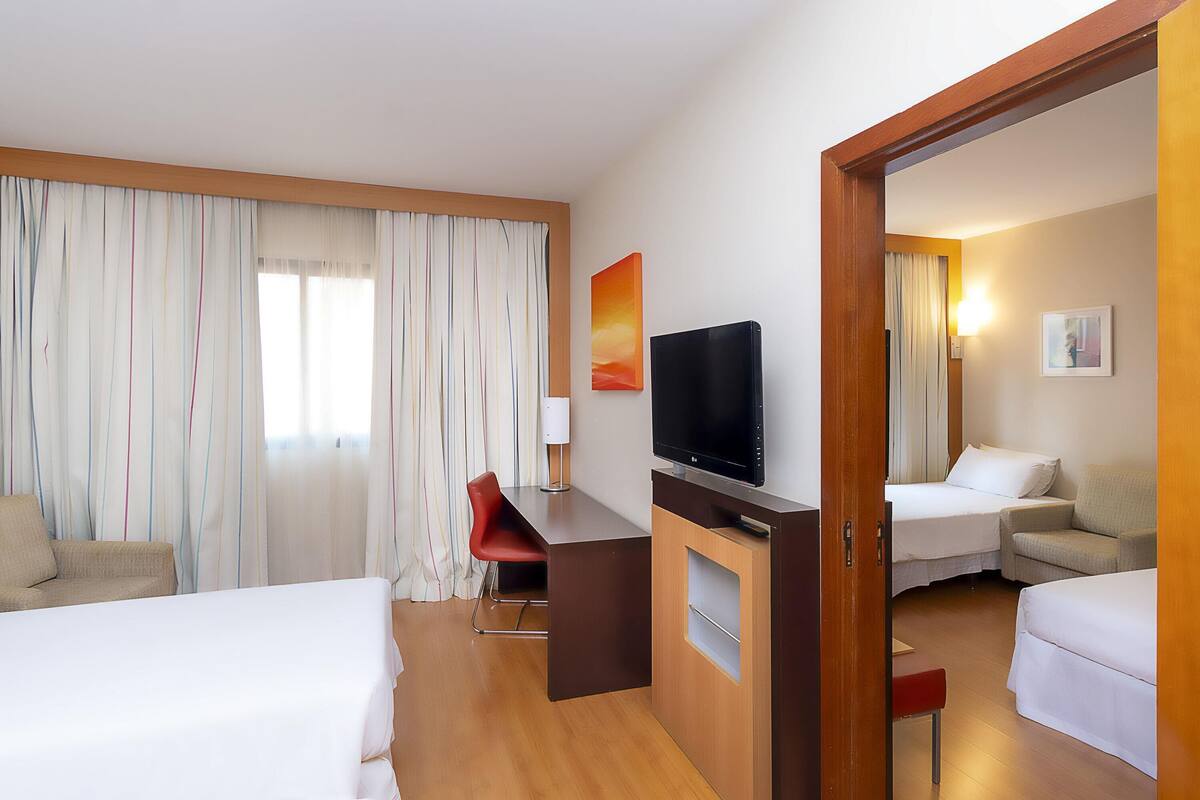 A hotel room with a bed, a desk with a TV, a chair, and a mirror.