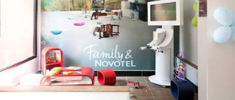 Zona de juegos infantiles con juguetes y equipo, un televisor y un letrero que dice "Family & Novotel".
