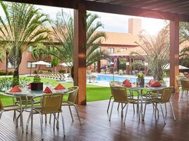 Un área de comedor al aire libre con mesas y sillas, una piscina y palmeras.