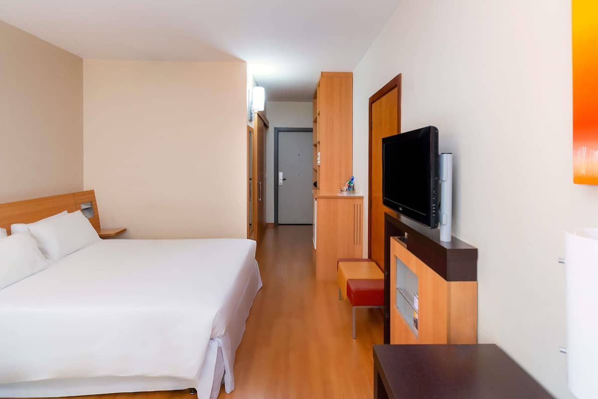A hotel room with a bed, a TV, a desk, and a door leading to a bathroom.