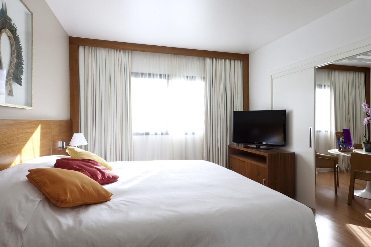 A hotel room with a bed, a TV, a desk, and a chair.