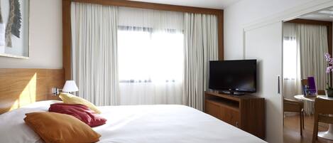 A hotel room with a bed, a TV, a desk, and a chair.