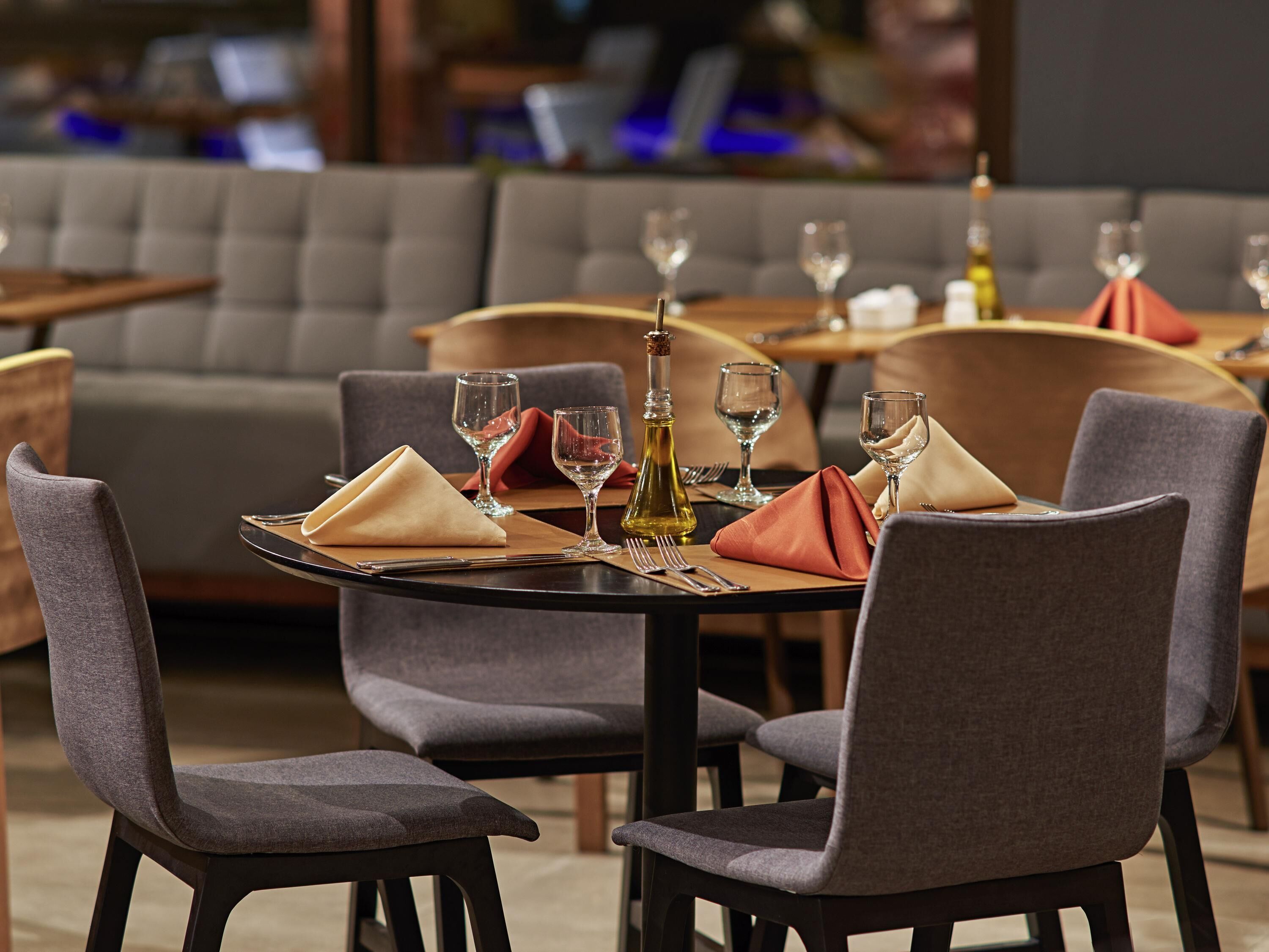 A dining area with tables set for two, each with a folded napkin, wine glass, and a bottle of olive oil.