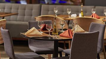 A dining area with tables set for two, each with a folded napkin, wine glass, and a bottle of olive oil.