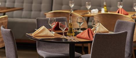 A dining area with tables set for two, each with a folded napkin, wine glass, and a bottle of olive oil.