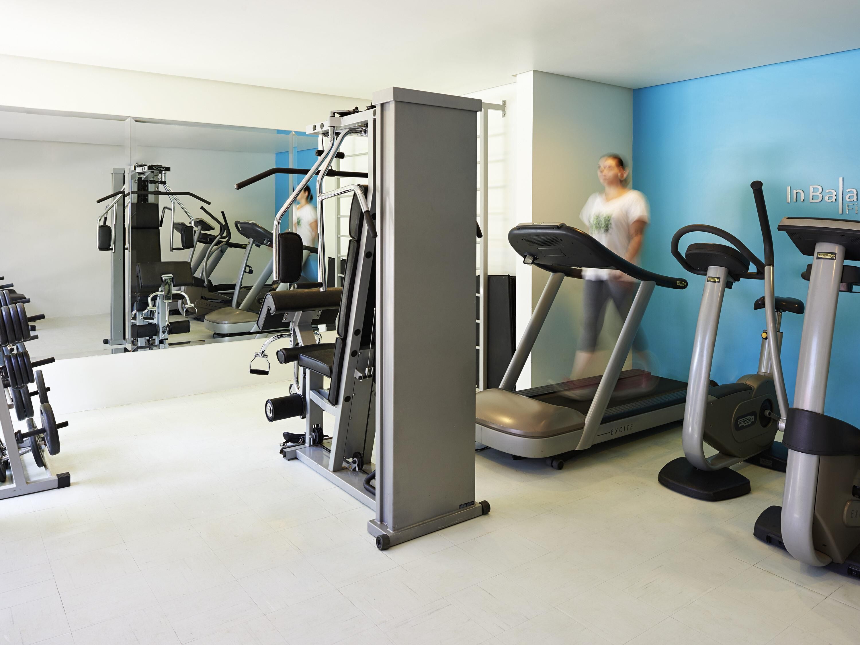 Une salle de sport équipée de matériel d’exercice, d’un tapis de course et d’un mur recouvert de miroirs.