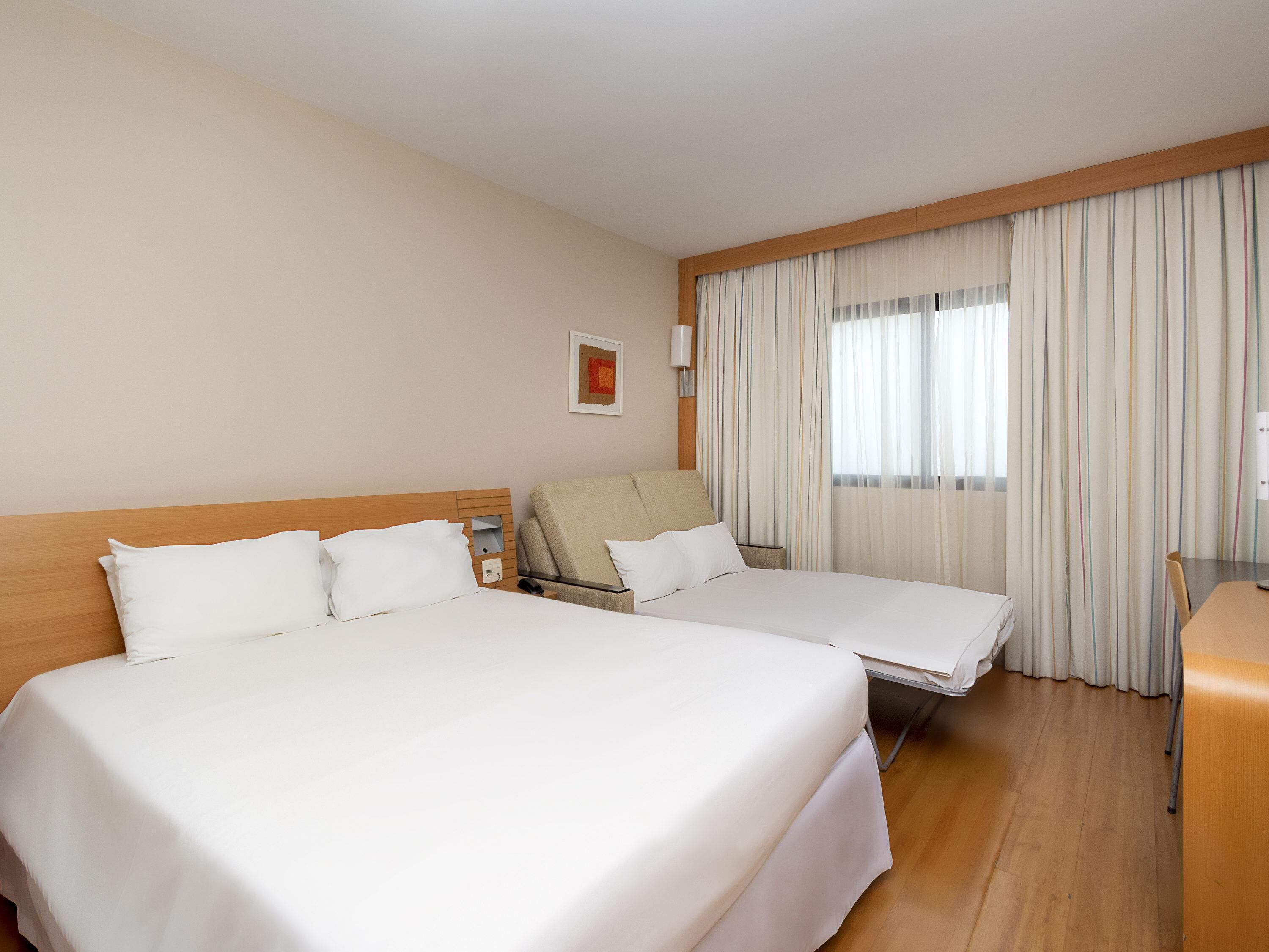A hotel room with two beds, a desk, a chair, and a window with curtains.
