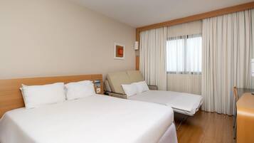 A hotel room with two beds, a desk, a chair, and a window with curtains.