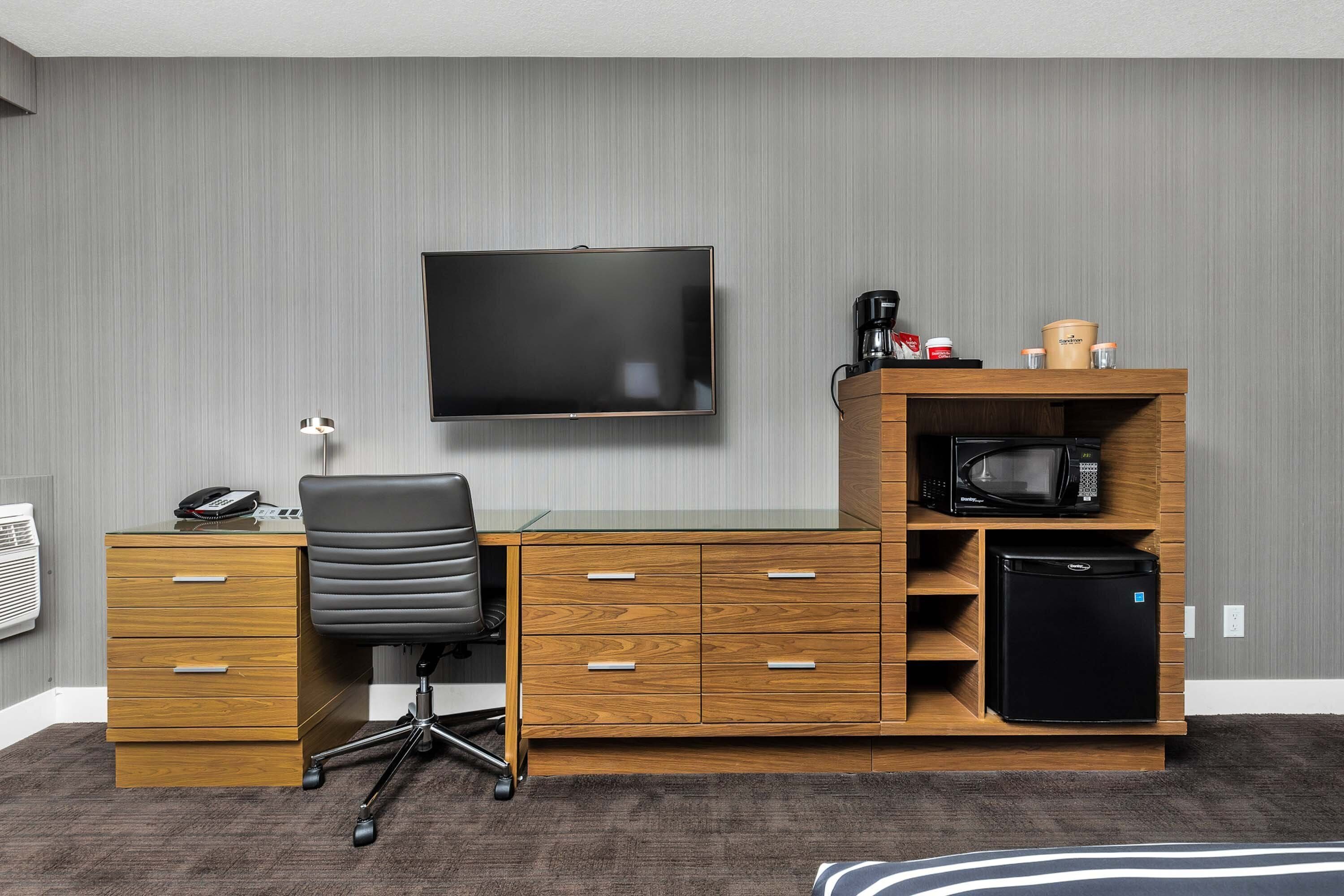 Un espace de bureau moderne avec un bureau en bois, un fauteuil de bureau noir et un téléviseur fixé au mur.