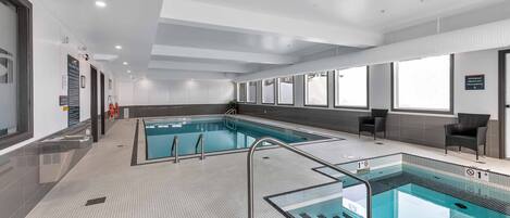 A modern indoor swimming pool with clear water, tiled flooring, and safety railings.