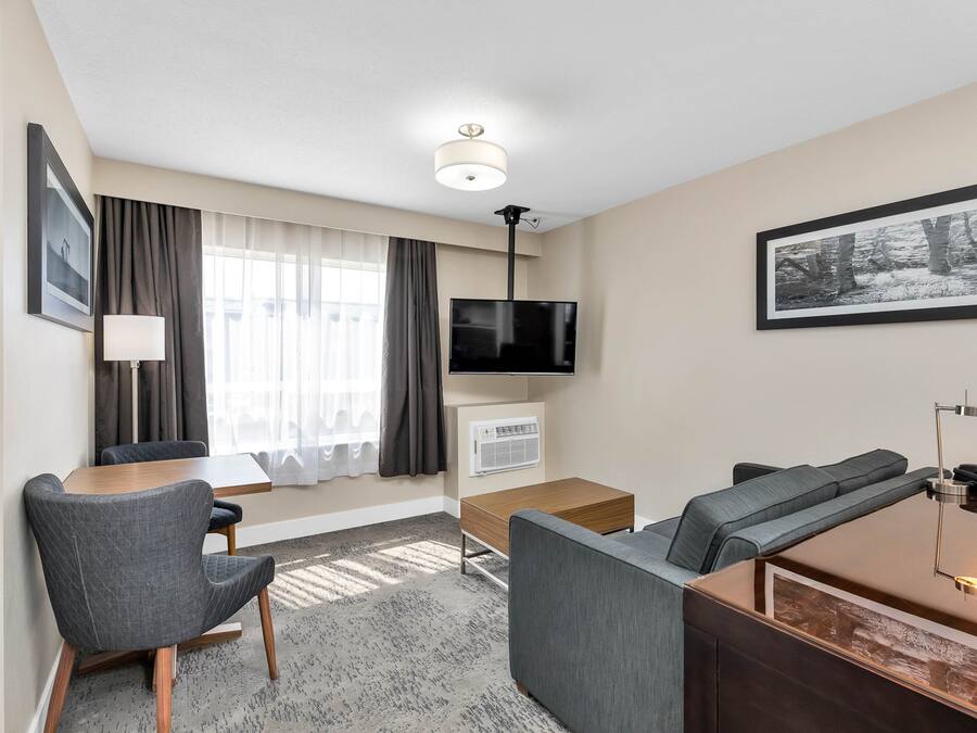 Habitació d'hotel moderna amb sofà, televisió, escriptori i finestra amb cortines.