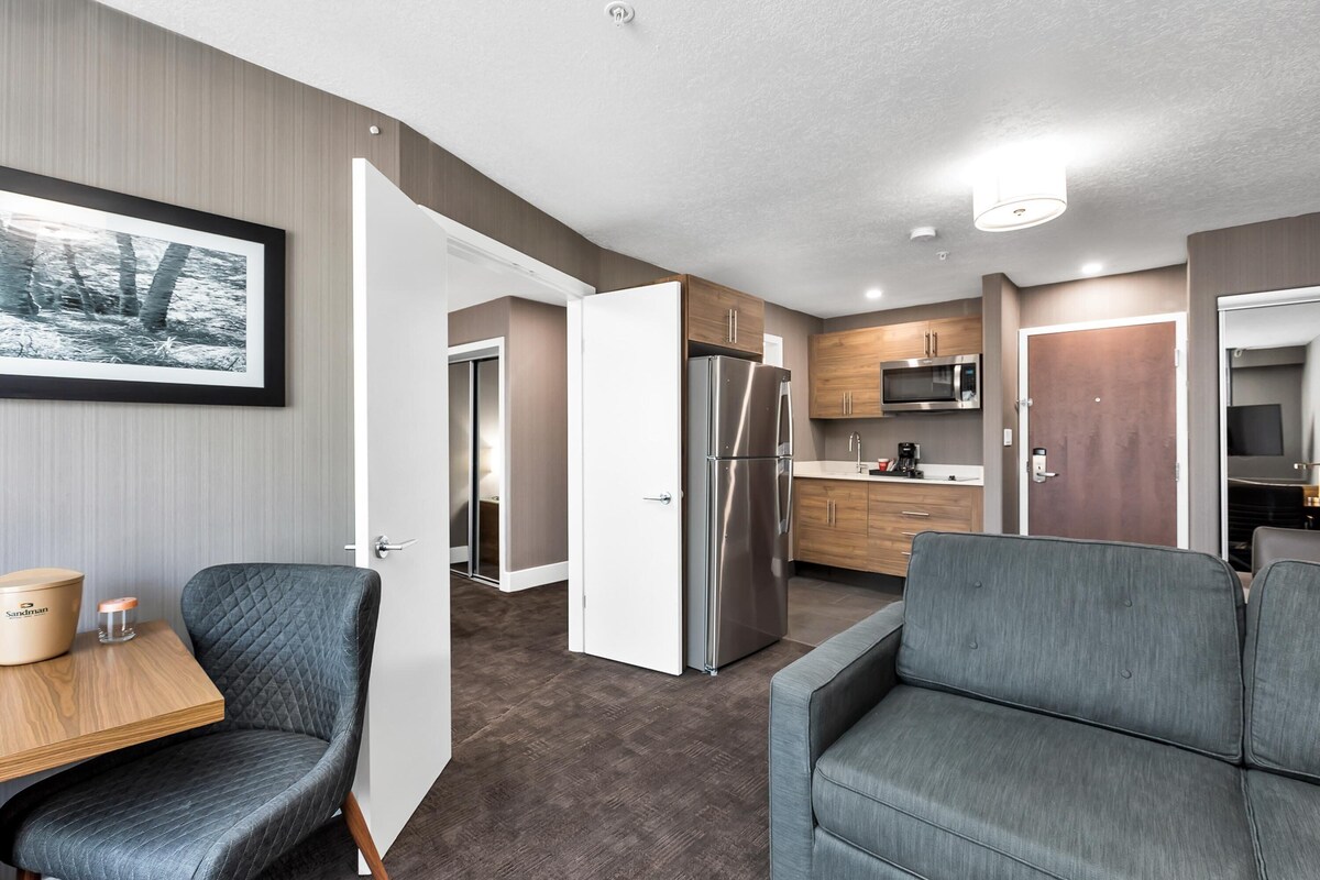 A modern kitchen with a refrigerator, microwave, and wooden cabinets. There is a dining area with a table and chairs.