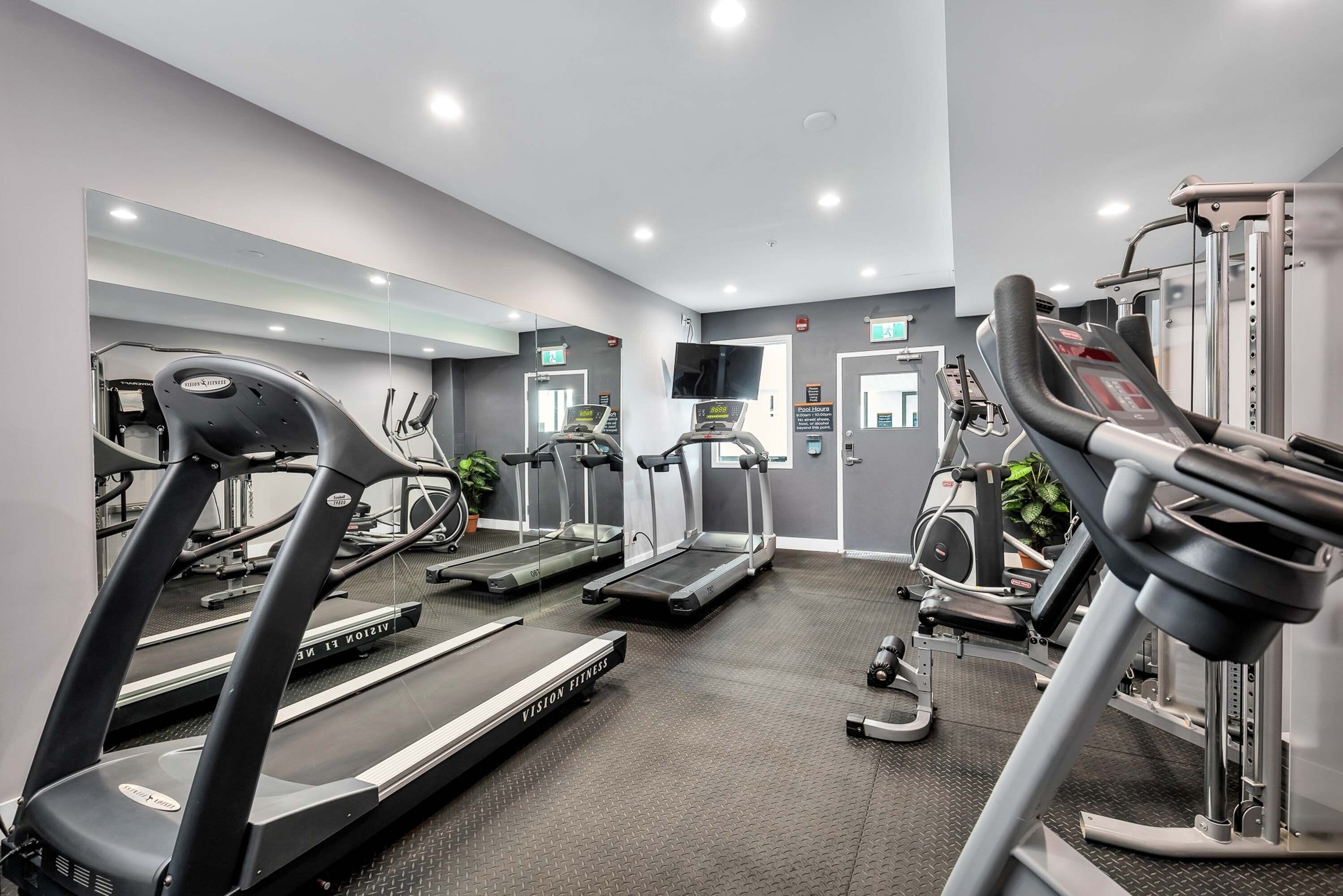 Une salle de sport équipée de tapis de course, de vélos elliptiques et d’appareils de musculation.
