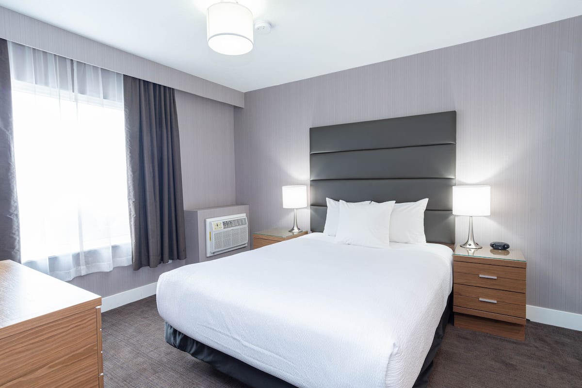 A modern hotel room with a large bed, bedside tables with lamps, a dresser, and a window with curtains.