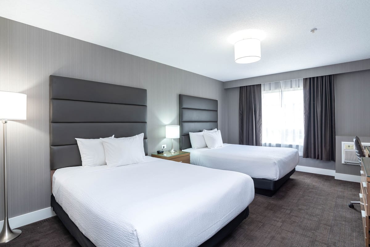A hotel room with two beds, a desk, a lamp, and a window with curtains.