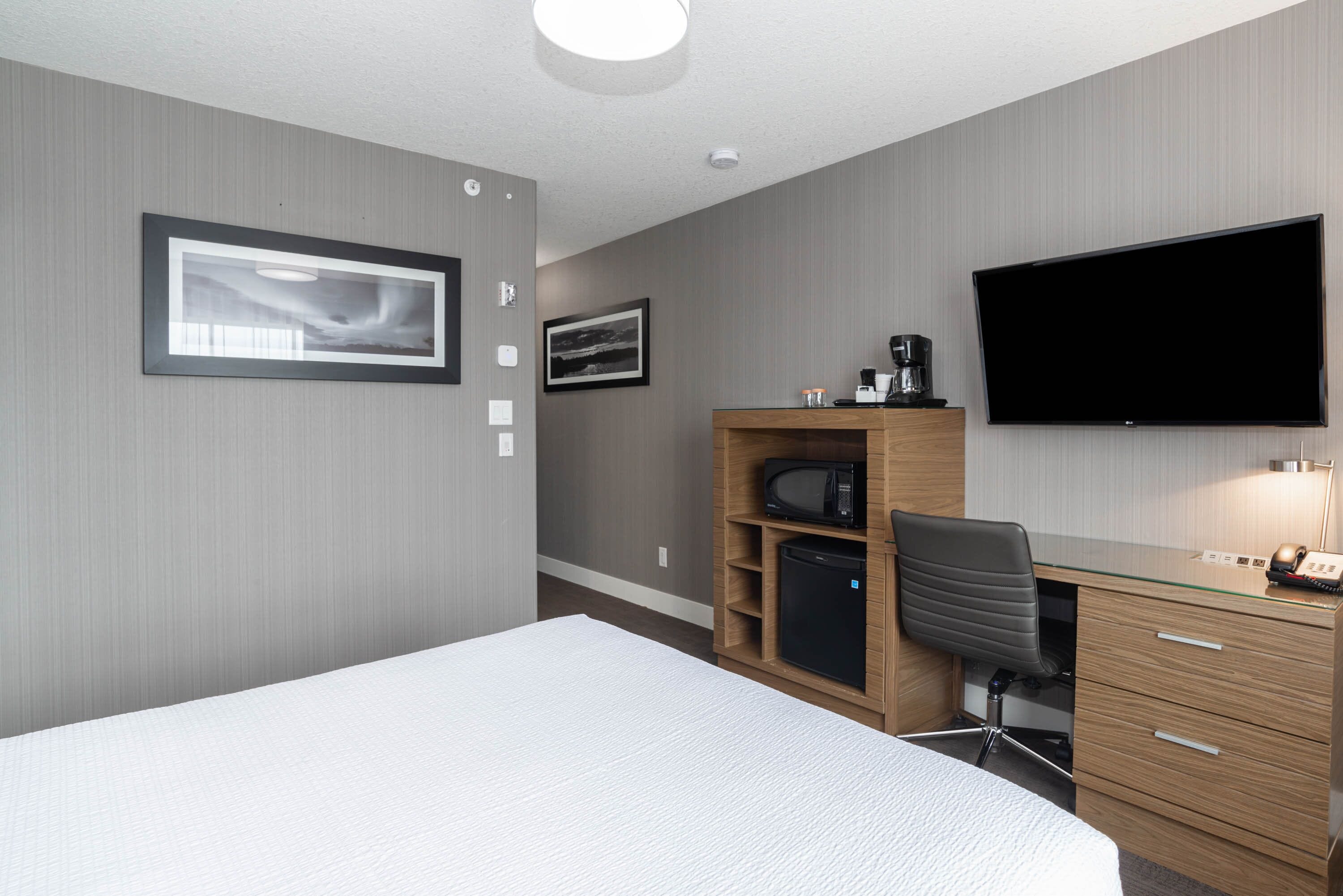 Une chambre d’hôtel équipée d’un lit, d’un bureau avec un ordinateur, d’une télévision et d’un four à micro-ondes.