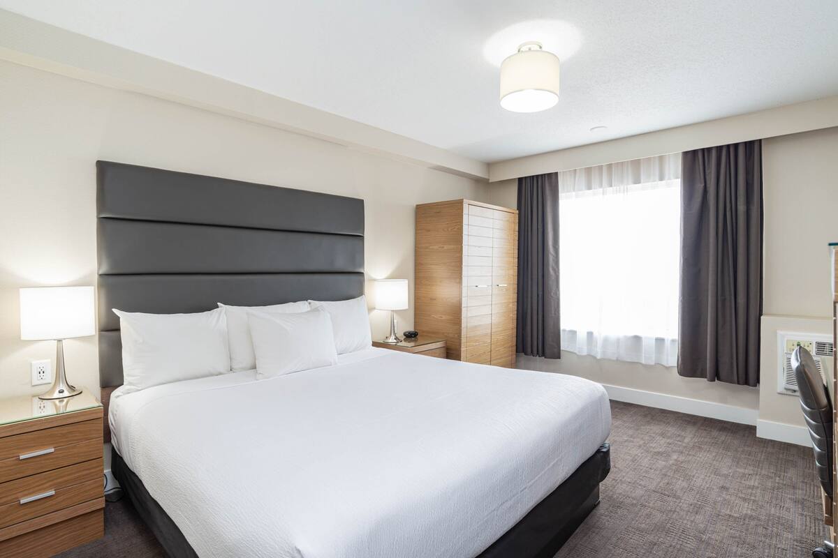 A modern hotel room with a large bed, bedside tables, a wardrobe, and a window with curtains.
