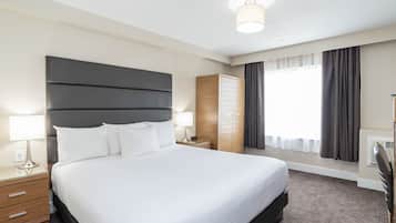 A modern hotel room with a large bed, bedside tables, a wardrobe, and a window with curtains.
