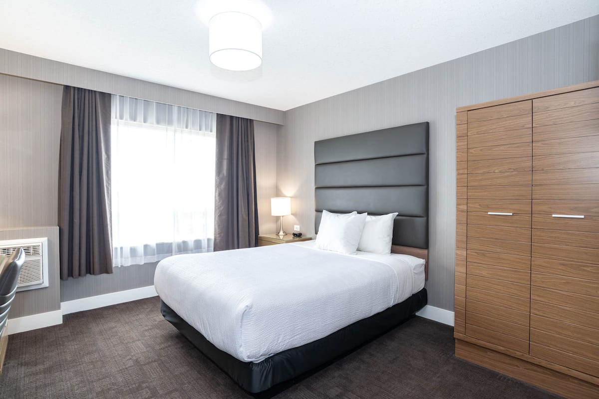 A hotel room with a large bed, a wardrobe, a desk, and a window with curtains.