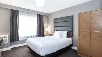 Quarto de hotel com uma cama grande, um guarda-roupa, uma escrivaninha e uma janela com cortinas.