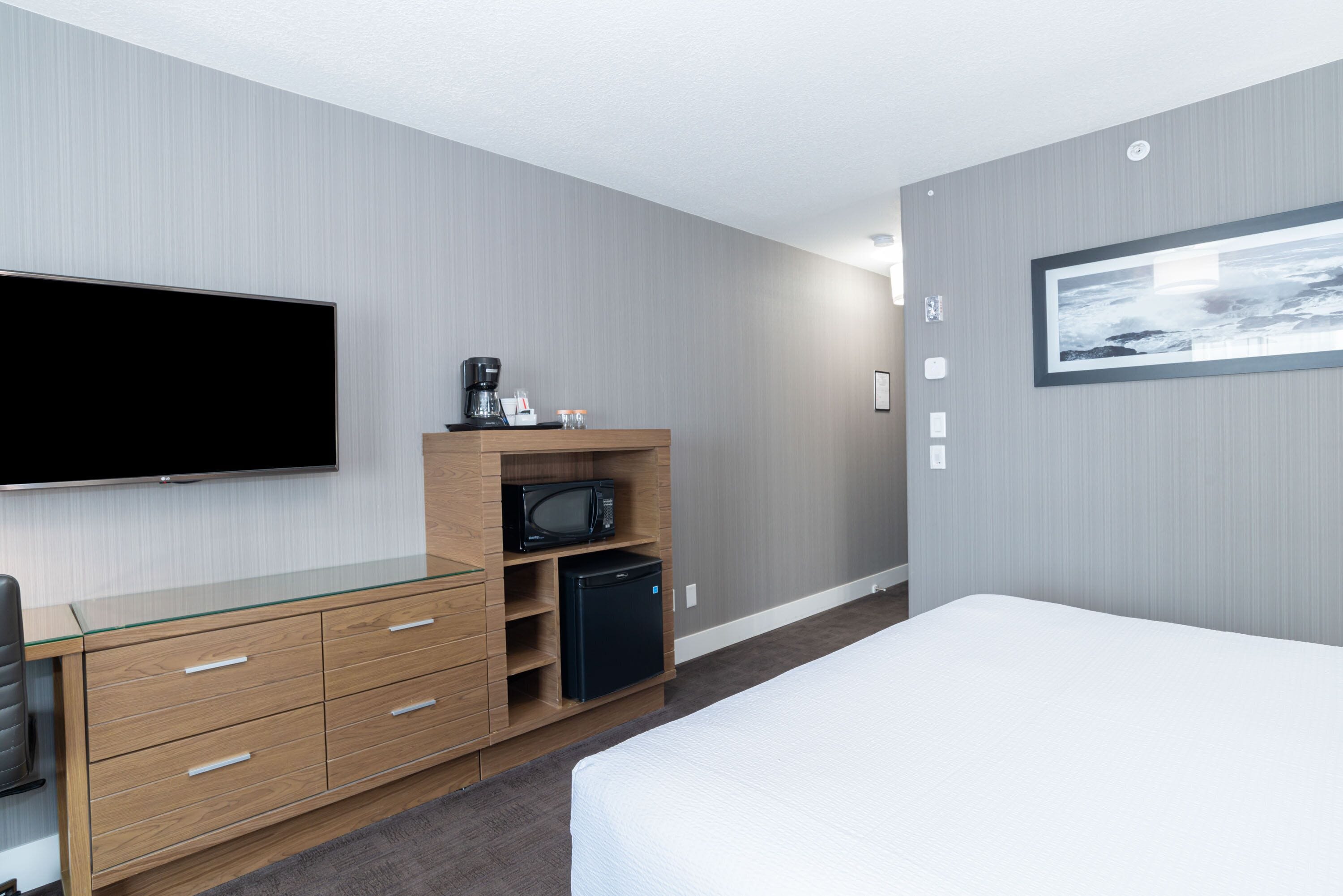 A modern hotel room with a flat-screen TV, a wooden dresser, a microwave, a coffee maker, and a bed.