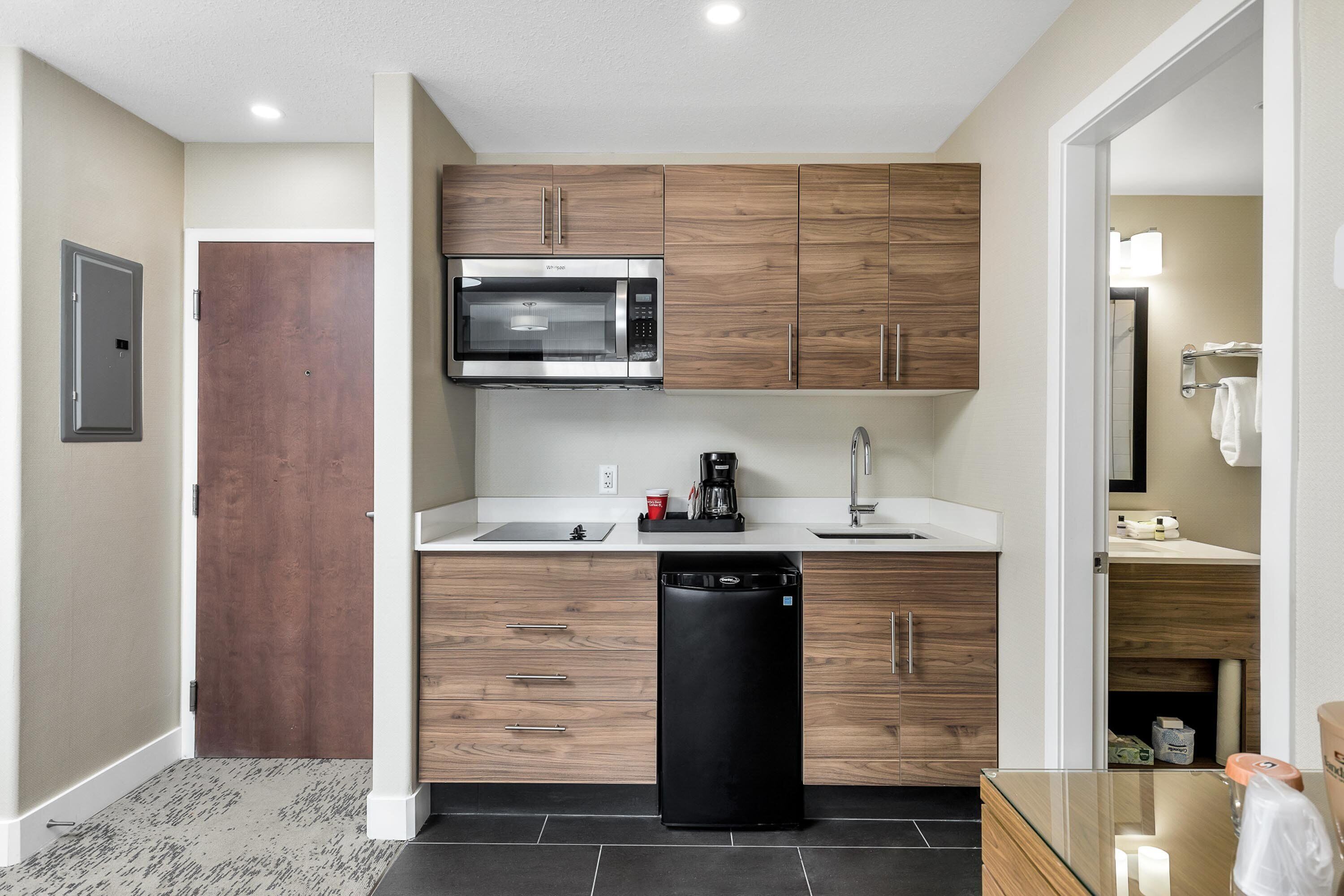 A compact kitchen with wooden cabinets, a built-in microwave, a coffee maker, and a dishwasher.
