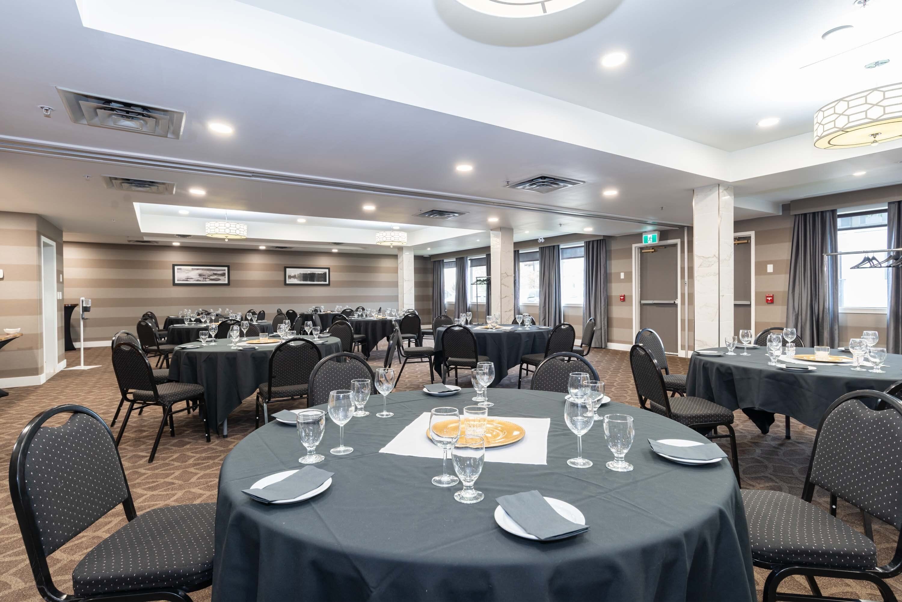A hotel conference room with multiple tables set for dining, equipped with chairs and dining ware.