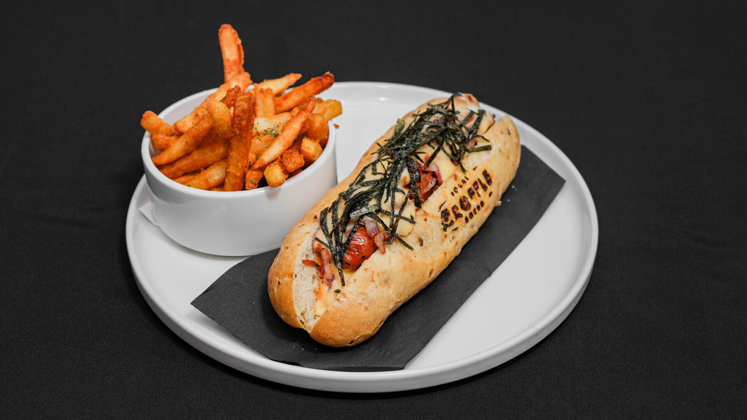 A hot dog with toppings and a side of fries on a white plate.