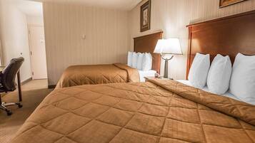A hotel room with two beds, a desk, a chair, and a lamp.