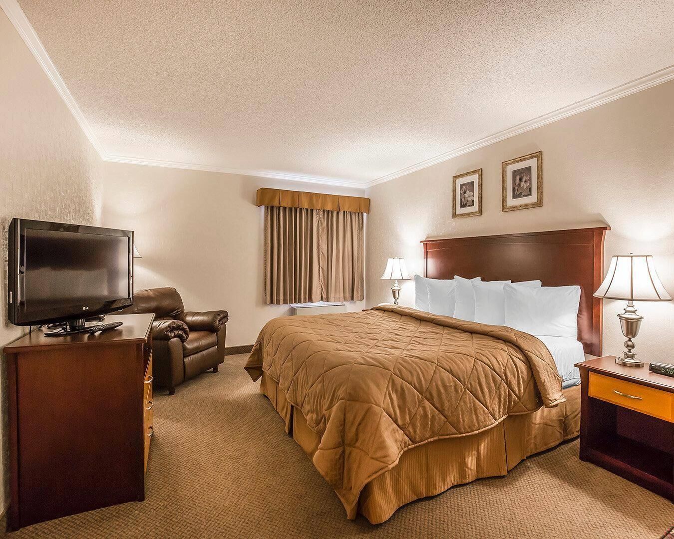A hotel room with a bed, a television, a desk, a chair, and a lamp.