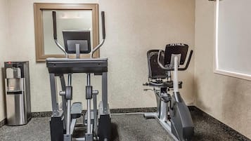Uma academia com bicicleta ergométrica, elíptico e bebedouro.