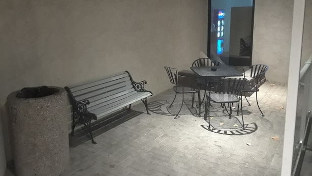 Un patio con un banco, una mesa con sillas y un cubo de basura.