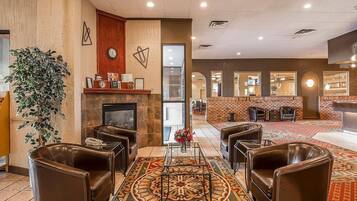 A hotel lobby with leather sofas, a patterned carpet, a fireplace, and a reception area with a counter and chairs.