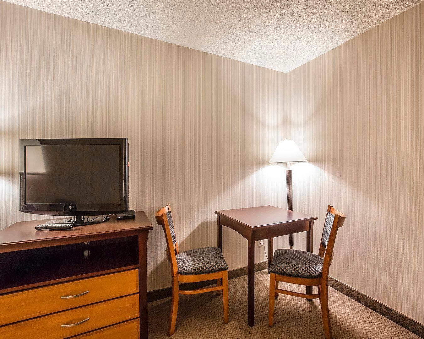 Une chambre d’hôtel équipée d’un bureau, d’une télévision, de deux chaises, d’une lampe et d’un sol recouvert de moquette.