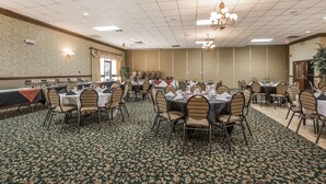 Un salón de banquetes con mesas dispuestas para comer, una alfombra estampada y una araña.