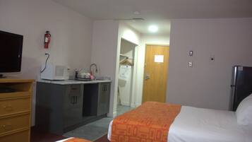 Habitación de hotel con cama, escritorio con microondas, kitchenette pequeña y armario.