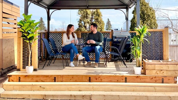 Een overdekt terras met een tafel, stoelen, een barbecue en potplanten.