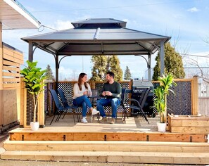 A covered patio with a table and chairs, a grill, and potted plants.