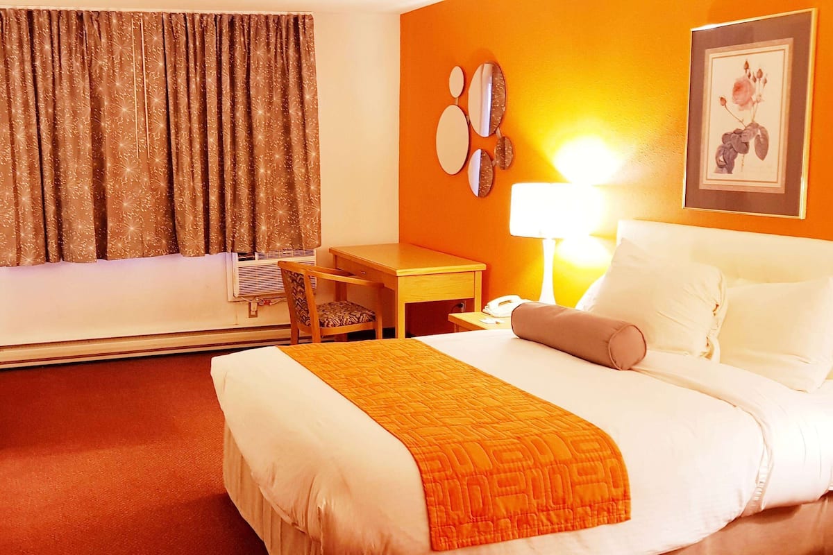 Une chambre d’hôtel comprenant un lit, un bureau, une chaise, une lampe et un mur orné d’un tableau encadré.