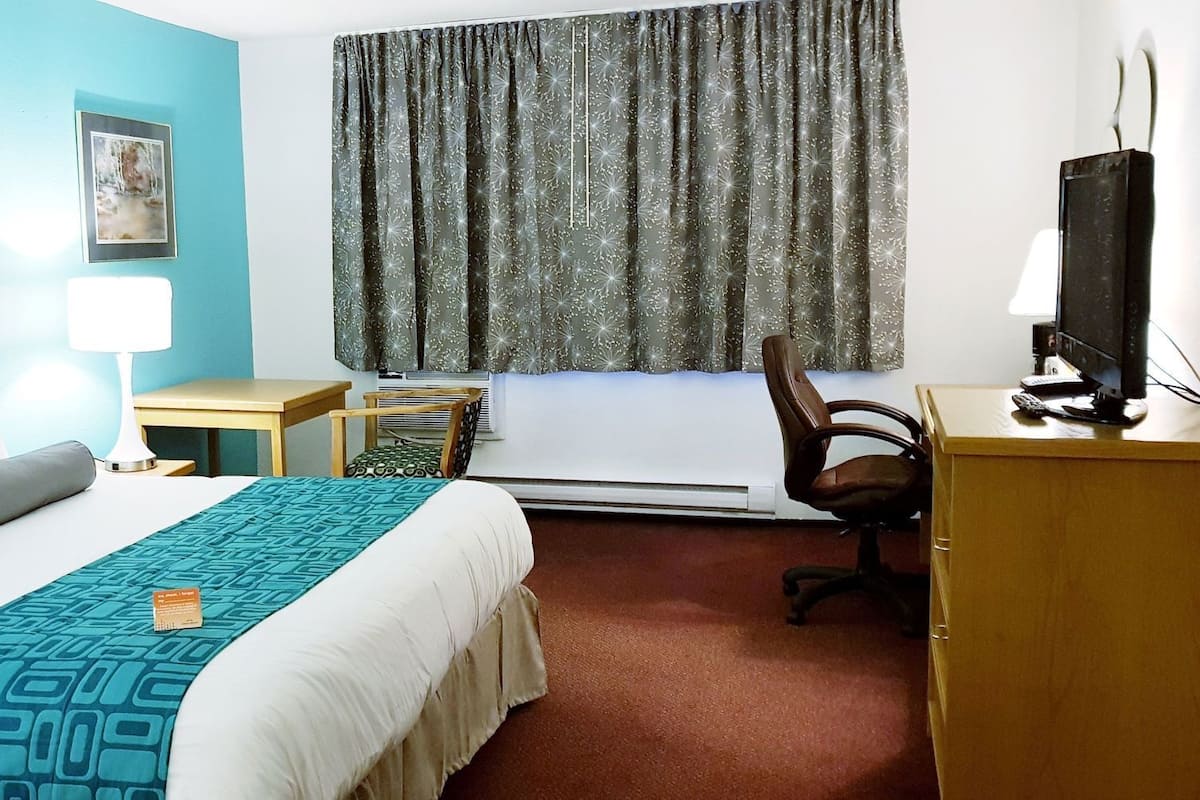 Une chambre d’hôtel équipée d’un lit, d’un bureau, d’une chaise, d’une télévision et de deux tableaux encadrés accrochés au mur.
