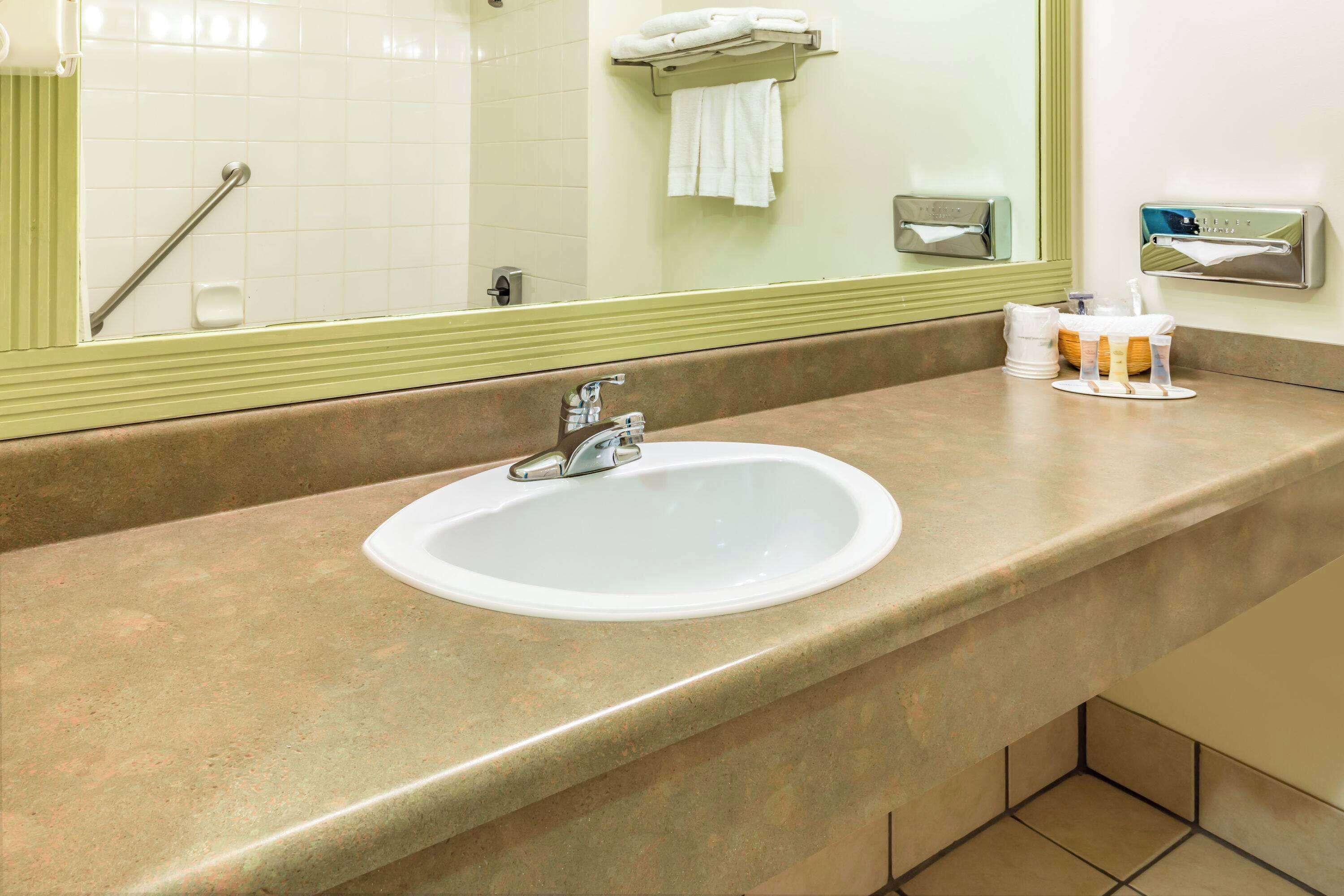 Une salle de bain équipée d’un lavabo, d’un miroir, d’un porte-serviettes et d’un distributeur de gel hydroalcoolique.