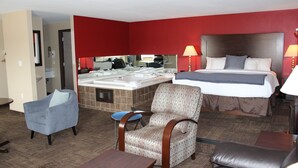 A hotel room with a bed, a chair, a small table, a sofa, a bathroom with a sink and mirror, and a red wall.