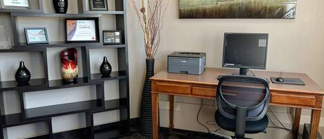 Un espacio de oficina moderno con un escritorio, una silla, un ordenador, una impresora y objetos decorativos en estanterías.