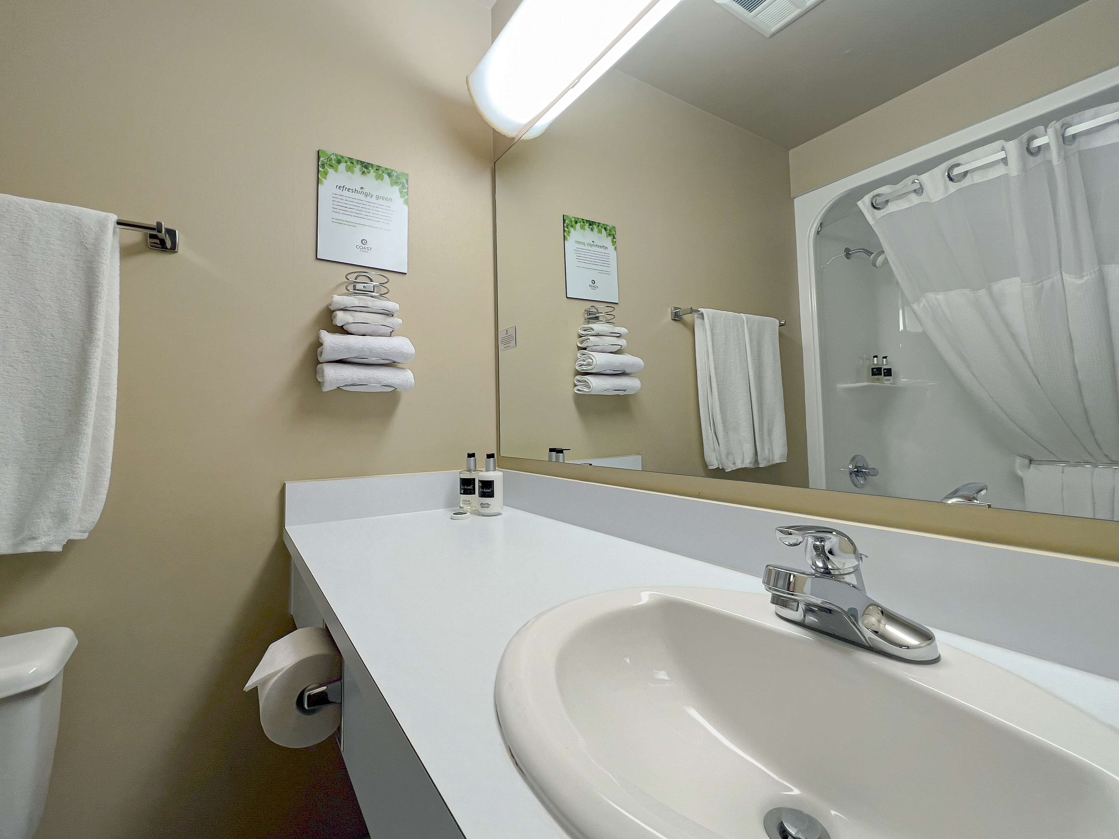 A bathroom with a white sink, a mirror, and multiple white towels hanging on hooks.