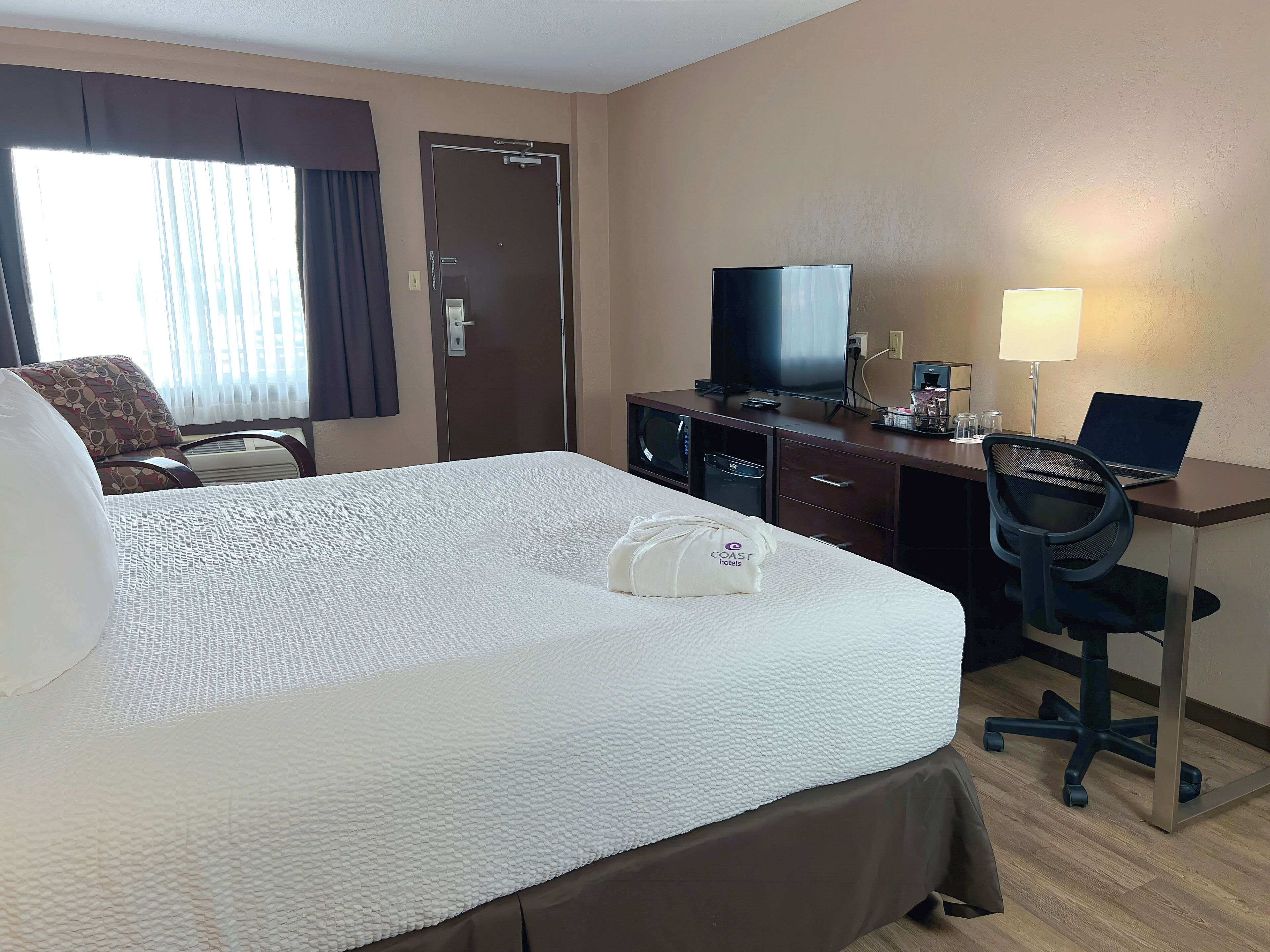 Habitación de hotel con una cama grande, un escritorio con una computadora portátil, un televisor y una silla.